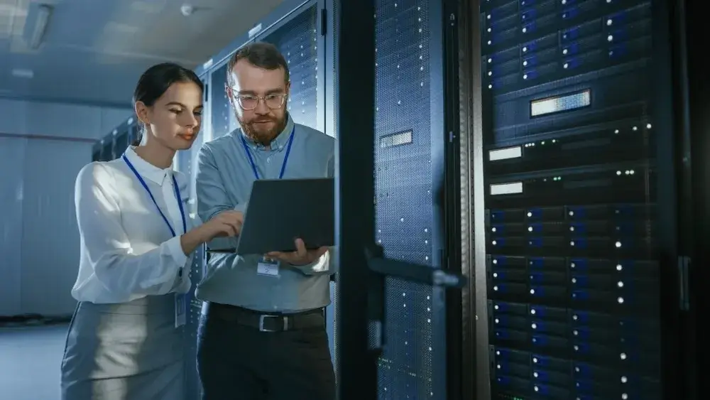 two employee watching status of server in laptop in a server room